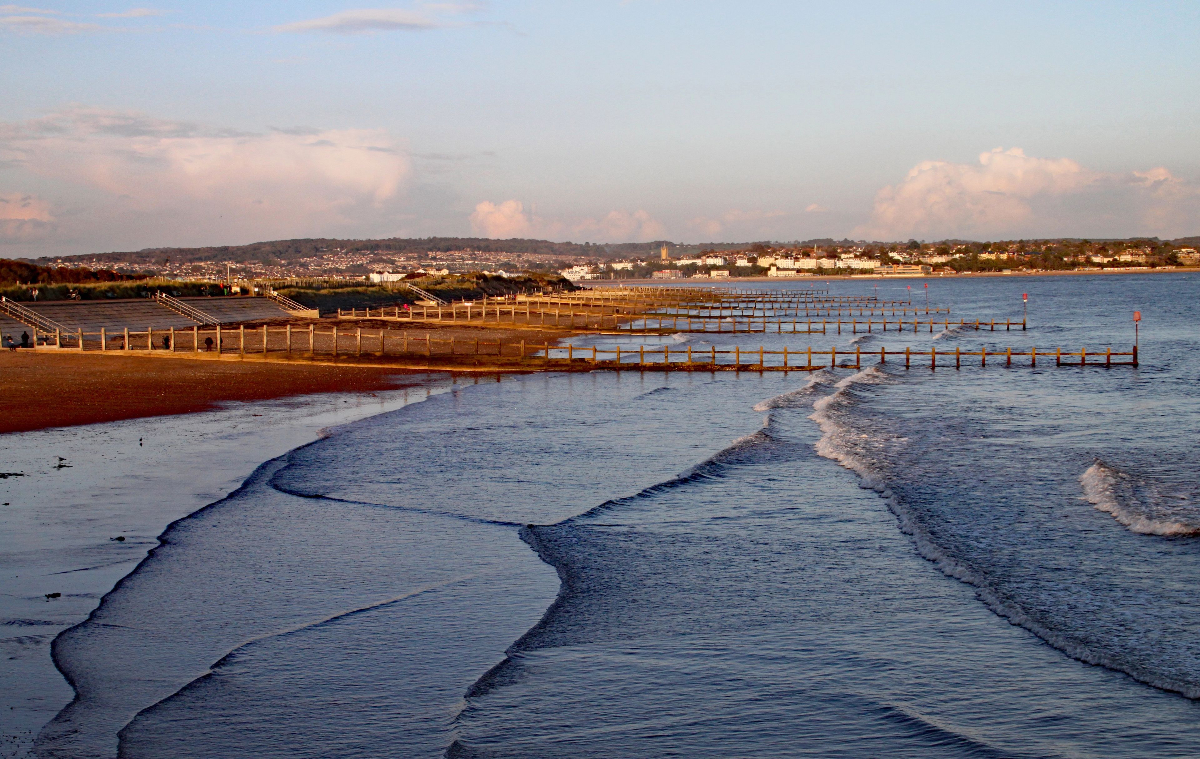 Golden hour coastal scene with gentle waves lapping against wooden groynes at sunset